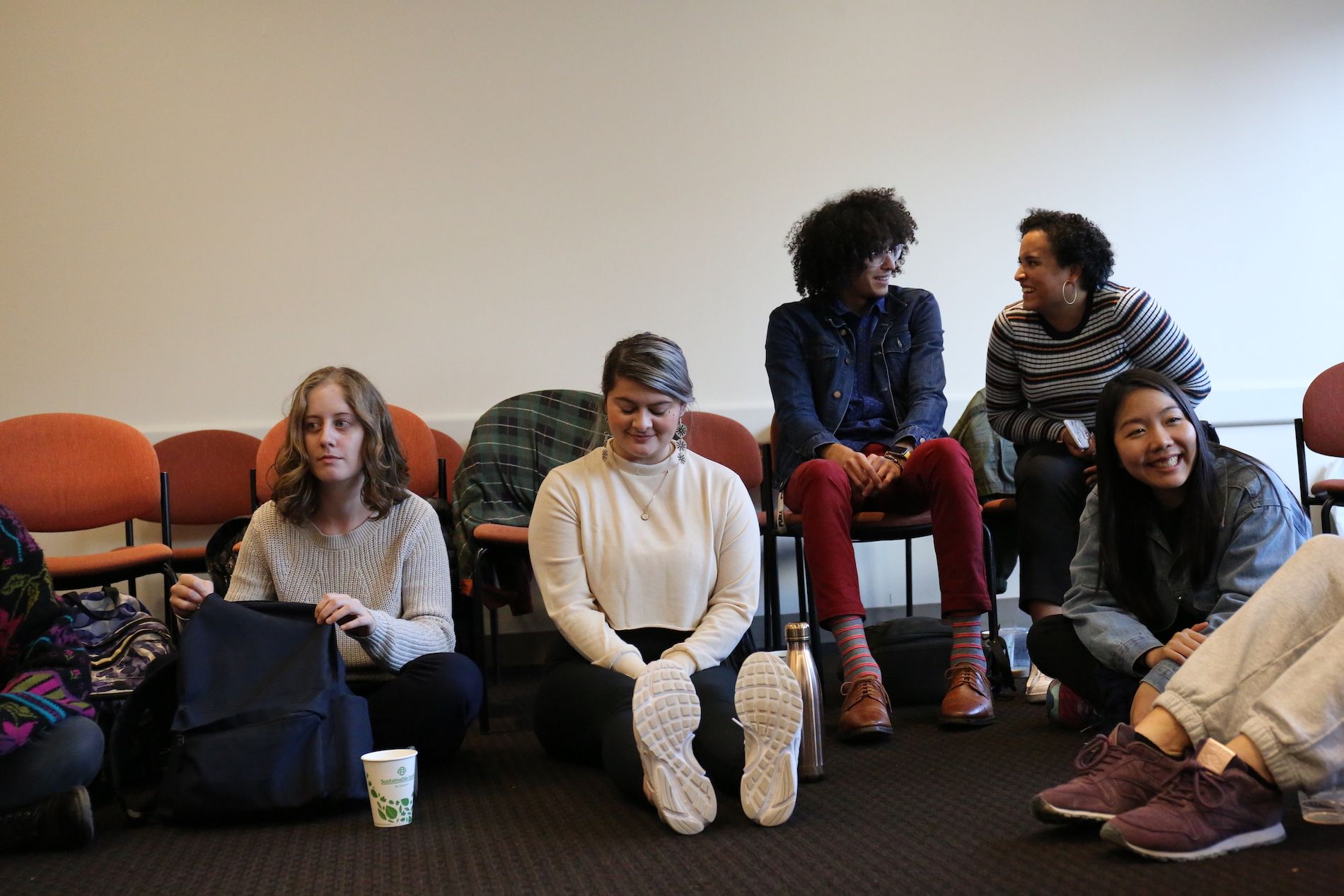 Five students sit in chairs and the floor in conversation